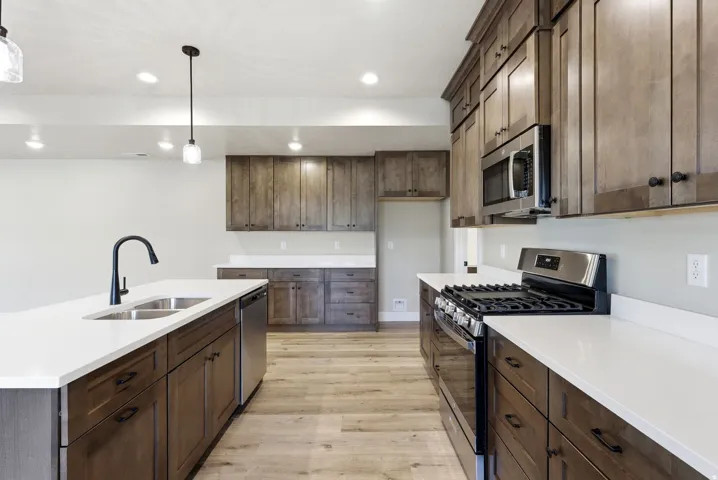 Wood-finish flooring, recessed lighting, and pendant lighting illuminate the kitchen