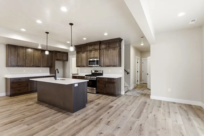 Open-concept kitchen featuring dark wood cabinetry, white countertops, stainless steel appliances, and a central island with a sink