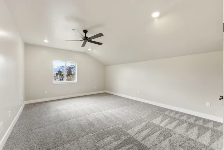 Spacious room featuring vaulted ceilings, recessed lighting, a ceiling fan, and window with exterior scenery