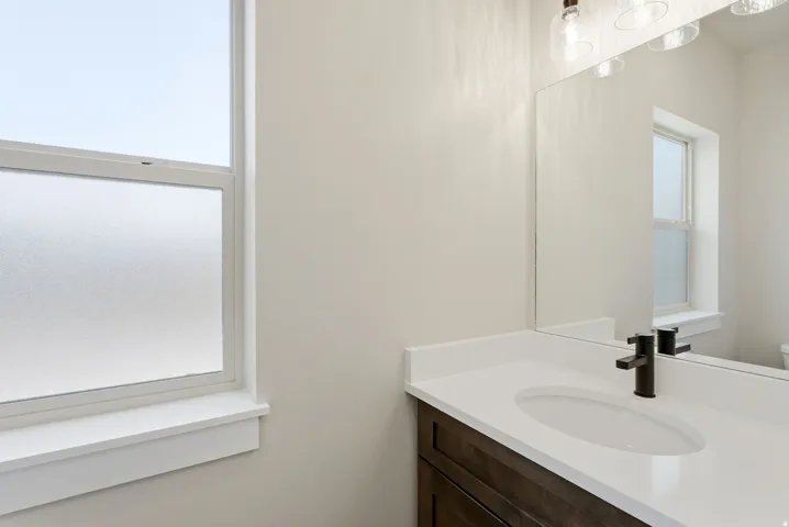 Frosted window, white countertop, dark wood-finish vanity, mounted mirror, and contemporary lighting fixture
