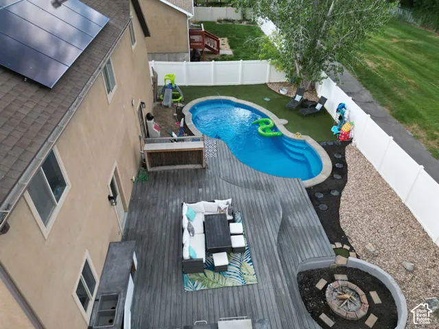 Outdoor living area featuring a custom-shaped inground pool, expansive wood-finish deck, fire pit, and solar panels