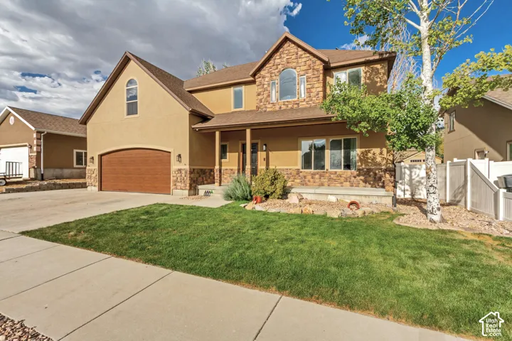 Stucco exterior with stone accents, covered front porch, arched window, attached garage, and concrete driveway