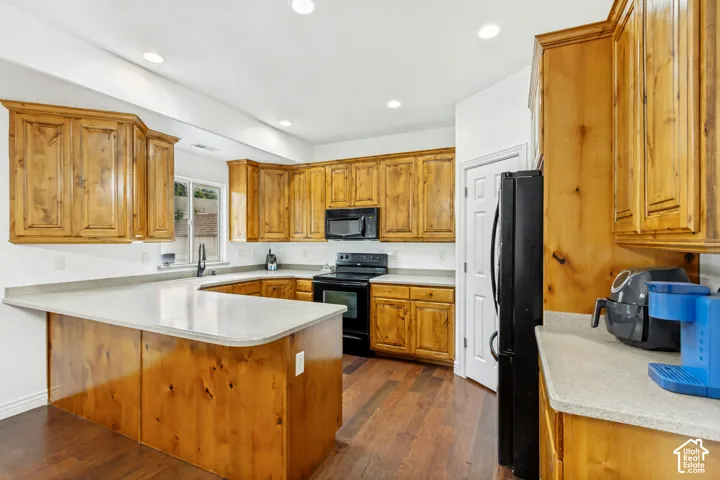 U-shaped kitchen with wood cabinetry, light-toned countertops, recessed lighting, and dark wood-finish flooring