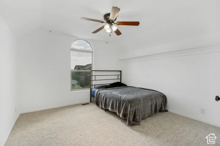 Arched window, ceiling fan, white walls, vaulted ceiling, and neutral carpet