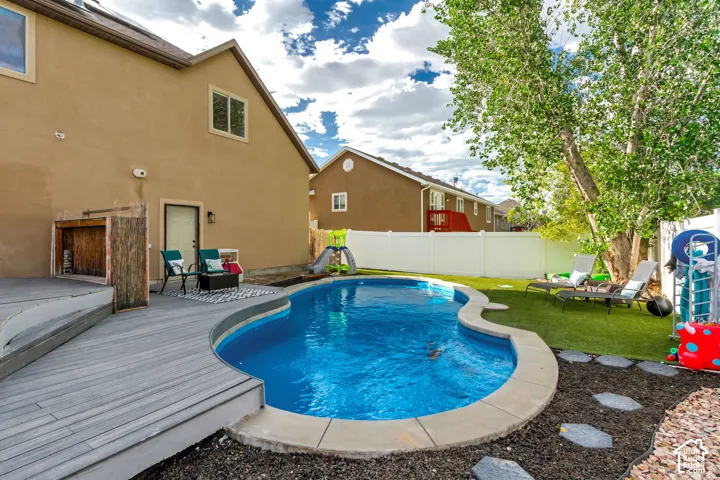 Curved swimming pool with concrete coping, composite decking, artificial turf, and a white vinyl fence