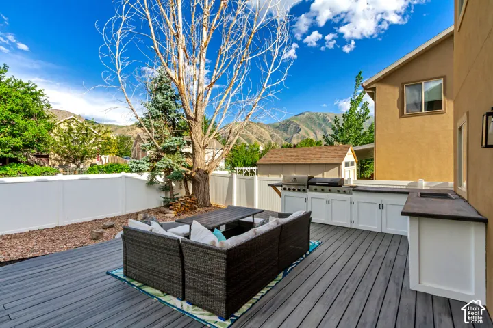Expansive outdoor deck featuring composite decking, a built-in outdoor kitchen with grill and sink, white cabinet storage, and a privacy fence