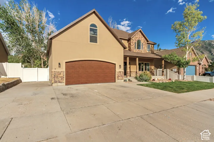 Stucco and stone facade, arched garage door, concrete driveway, front porch, and established landscaping