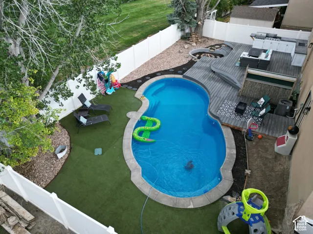 Custom-shaped swimming pool with stone coping, composite deck, built-in outdoor kitchen, and synthetic turf lawn