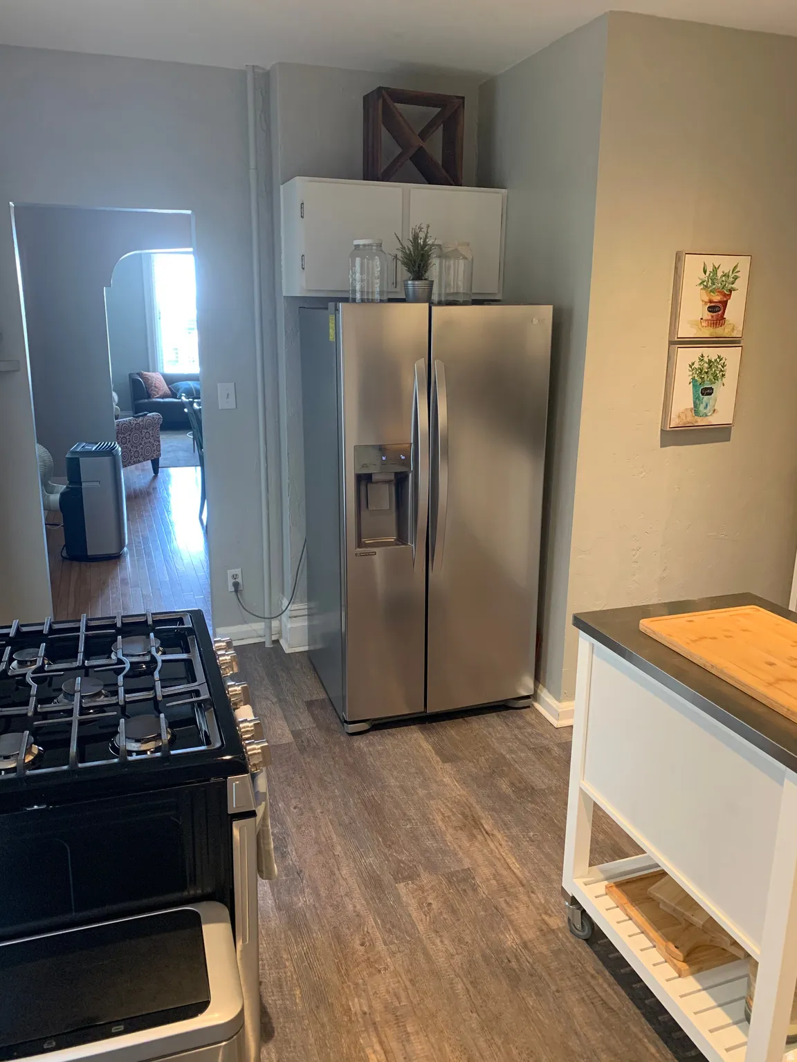 Stainless steel French door refrigerator, white upper cabinetry, wood-finish flooring, and a gas range