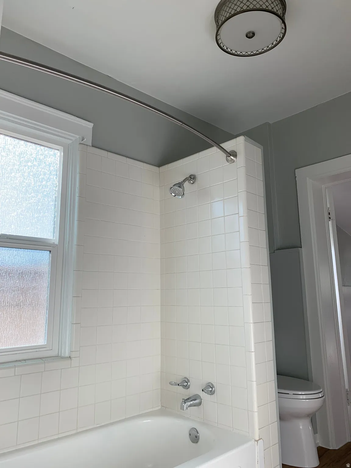 White subway tile bath surround, chrome fixtures, frosted glass window, and a ceiling-mounted light fixture