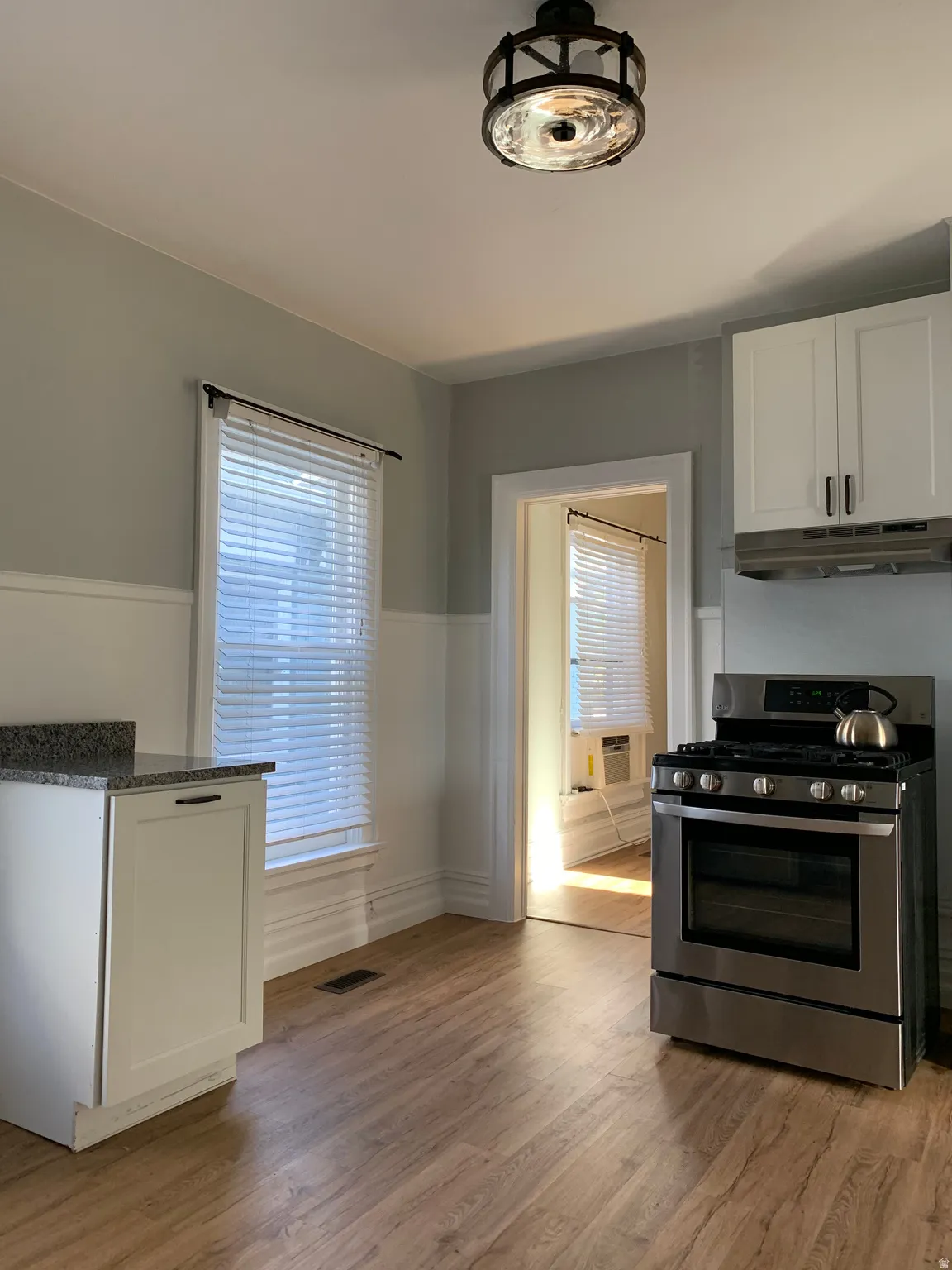 Wood-finish flooring, white cabinetry, stainless steel range, and granite-look countertop