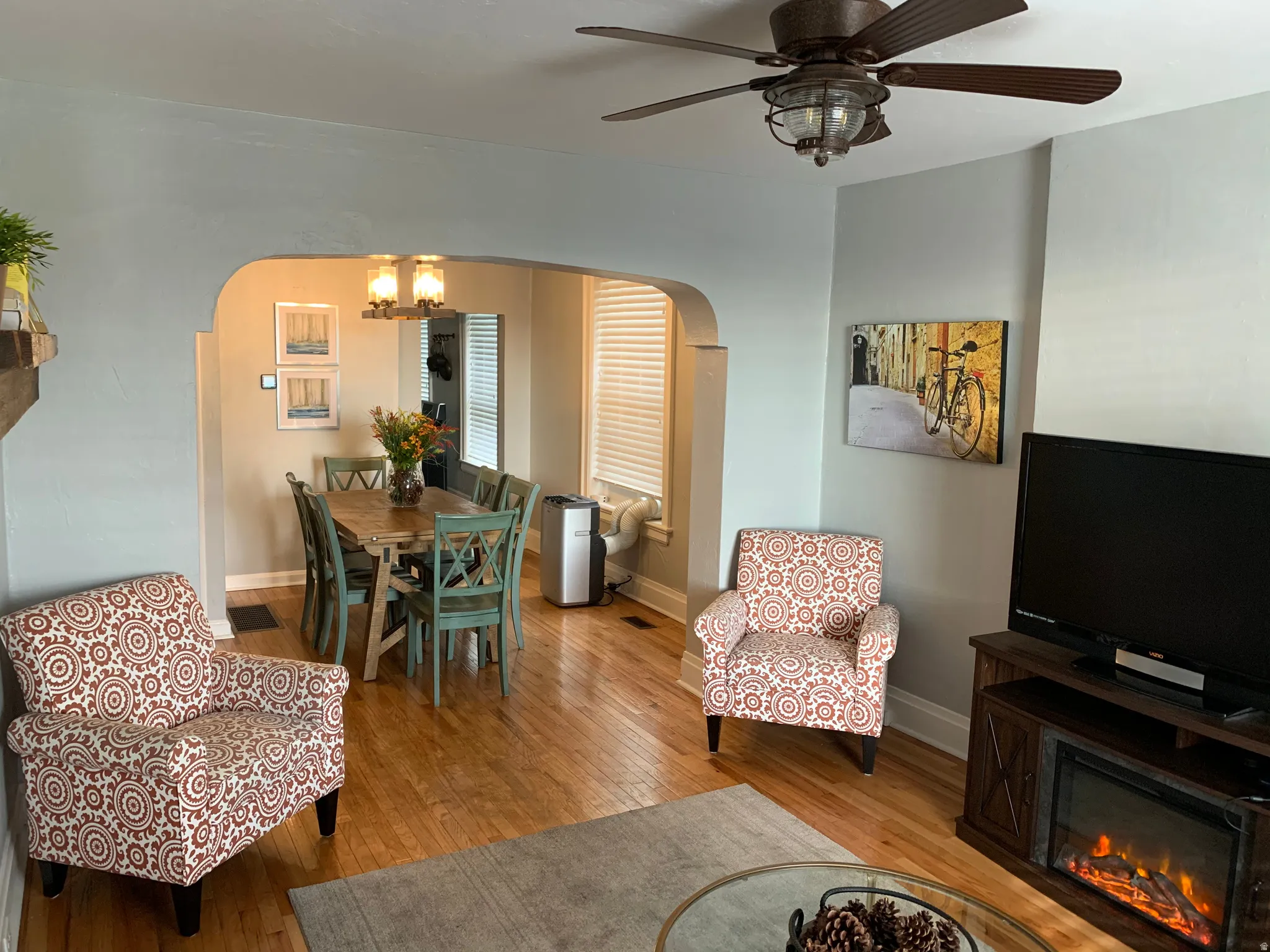 Hardwood-finish flooring, recessed archway, ceiling fan with integrated lighting, built-in fireplace, and overhead dining area lighting
