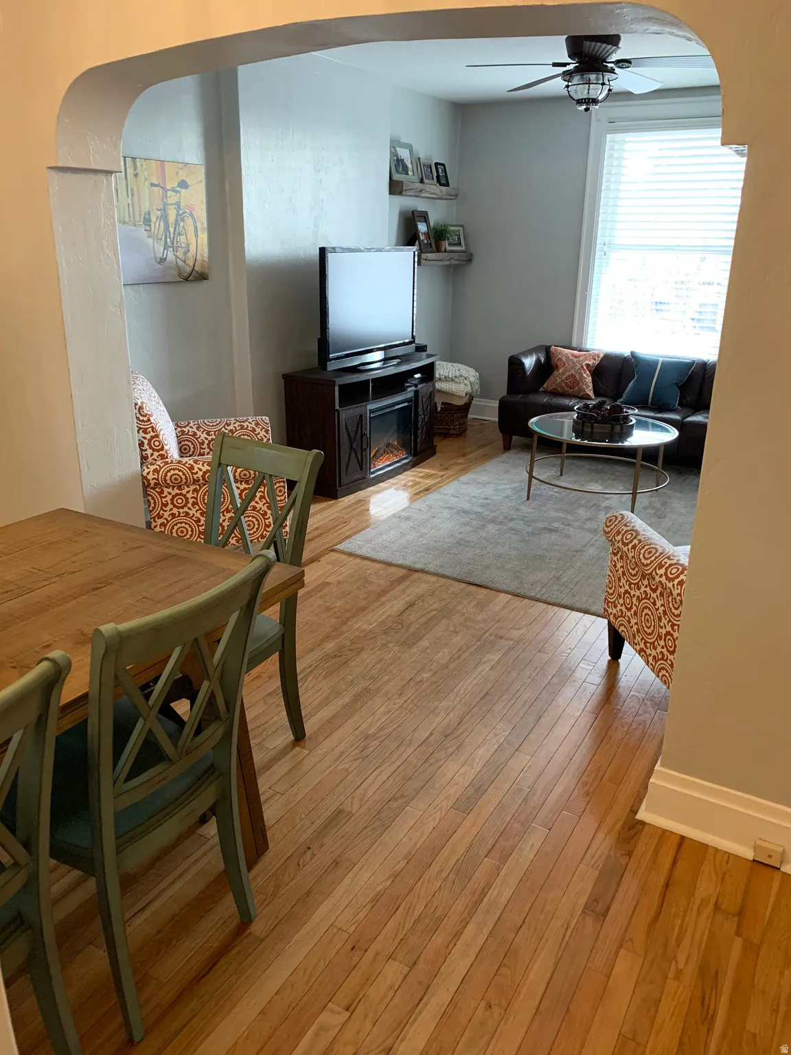 Archway opening, wood-finish flooring, ceiling fan with light fixture, window with blinds, wall-mounted shelving