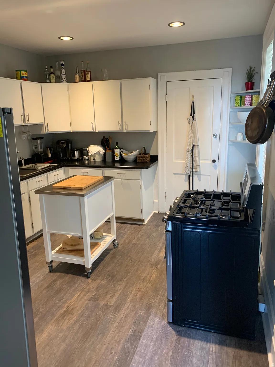 Kitchen featuring wood-finish flooring, white cabinetry, black countertops, and recessed lighting