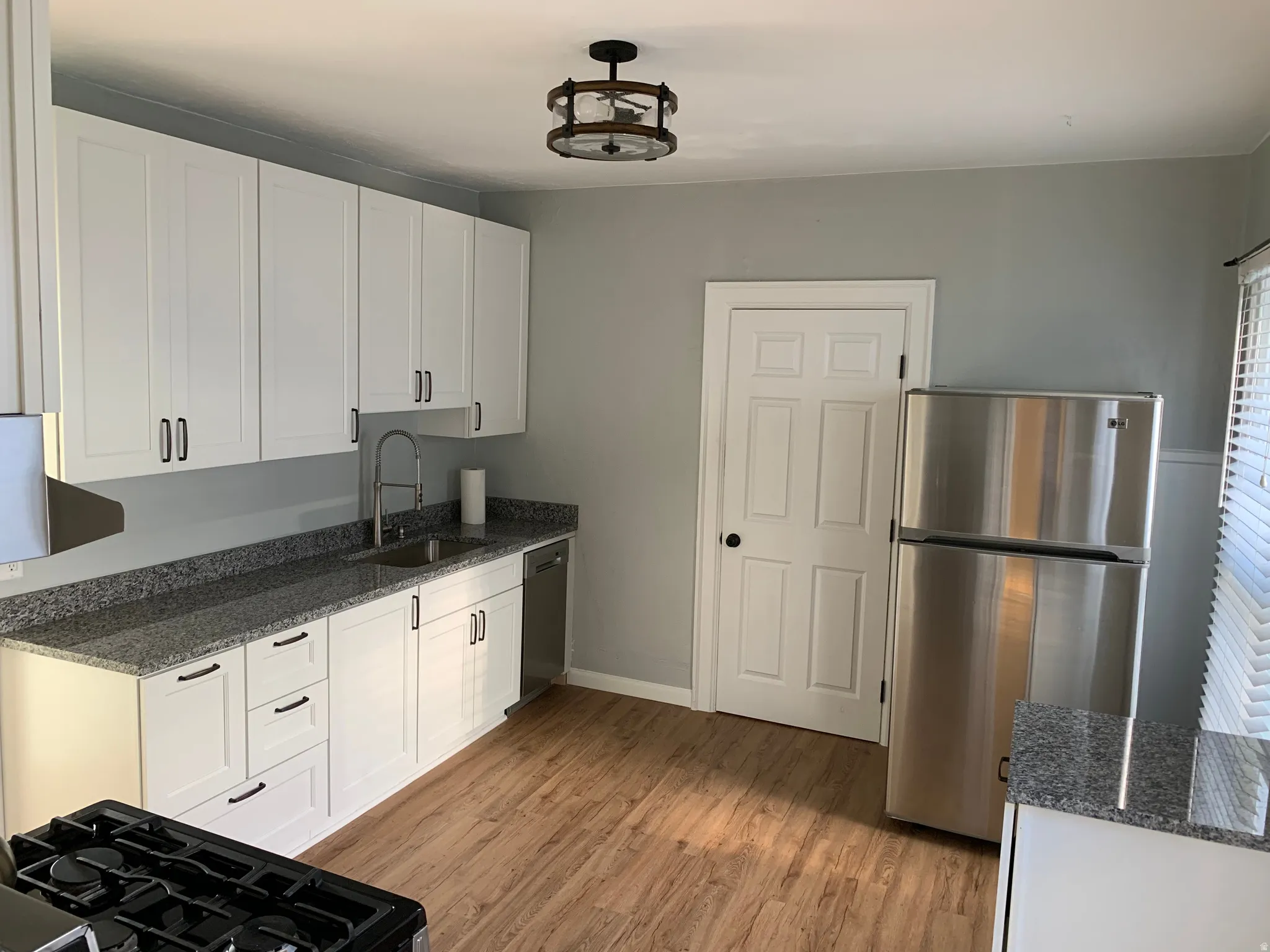White shaker cabinetry, granite-finish countertops, stainless steel appliances, wood-finish flooring, and a contemporary ceiling light fixture