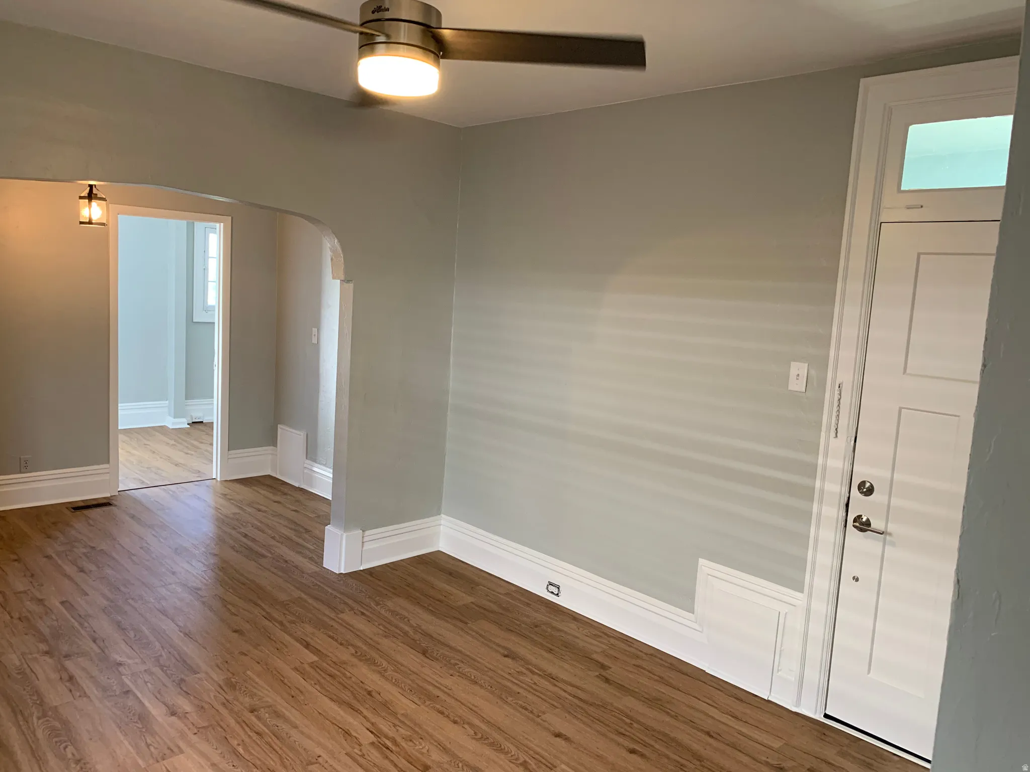 Wood-finish flooring, ceiling fan with integrated lighting, white trim, and a paneled entry door with transom