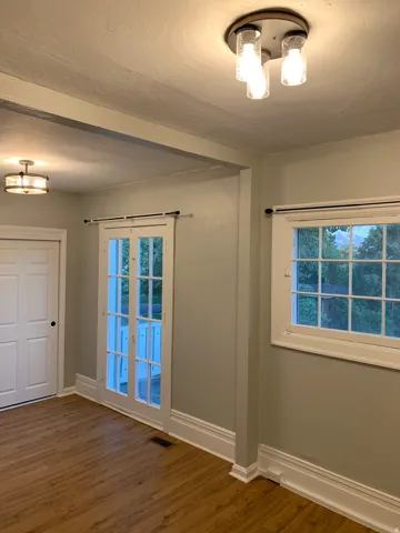 Wood-finish flooring, white window trim, white baseboards, and white paneled doors