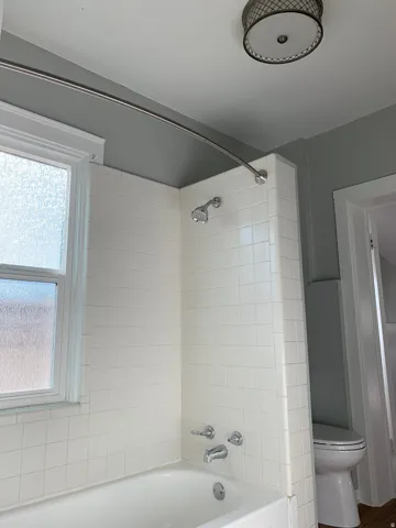 White subway tile bath surround, chrome fixtures, frosted glass window, and a ceiling-mounted light fixture