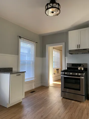 Wood-finish flooring, white cabinetry, stainless steel range, and granite-look countertop