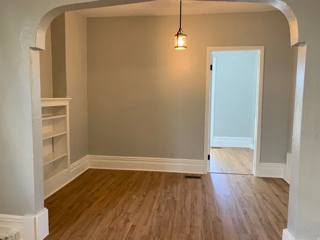 Wood-finish flooring, built-in shelving, decorative archway, traditional baseboards, and a pendant light fixture
