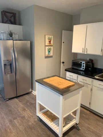 Wood-finish flooring, white cabinetry with silver hardware, and a mobile kitchen island with a stainless steel top