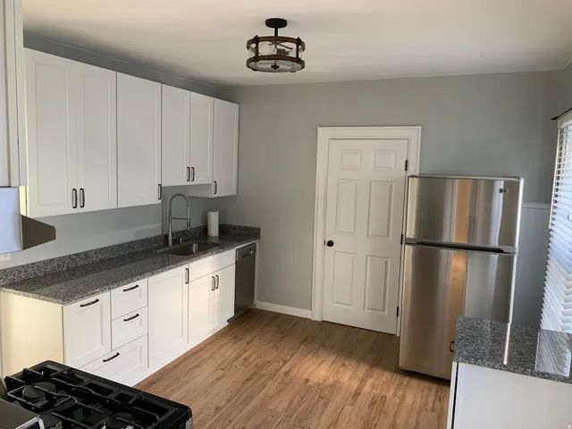 White shaker cabinetry, granite-finish countertops, stainless steel appliances, wood-finish flooring, and a contemporary ceiling light fixture