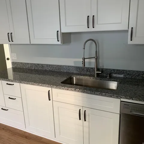 White shaker-style cabinetry with dark hardware, stainless steel undermount sink, gooseneck faucet, and speckled gray countertops