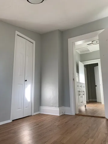 Wood-finish flooring, white bi-fold closet doors, white baseboards, and a flush-mount ceiling light fixture