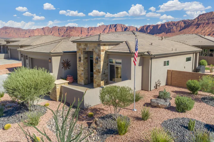 Stucco exterior featuring a stone accent entry, tile roof, and desert landscaping with gravel and native plantings