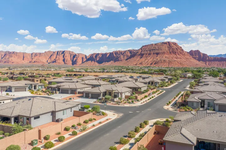 Residential street with uniform tile roofs, desert landscaping, and a backdrop of red rock formations