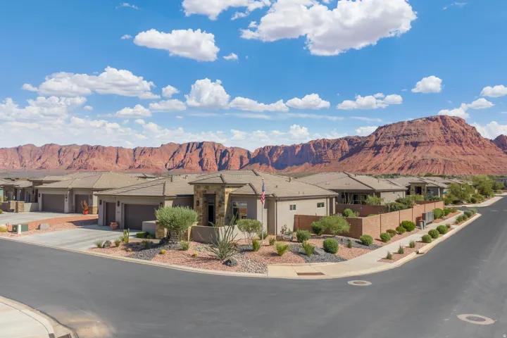 Desert landscape featuring a corner lot with mature landscaping, a stone-accented exterior, an attached garage, and a tiled roof