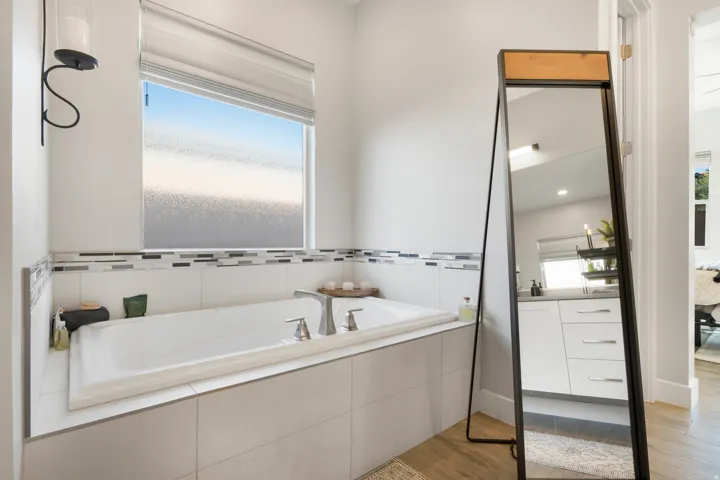 White-tiled soaking tub with a mosaic tile accent, large frosted window, and brushed nickel fixtures