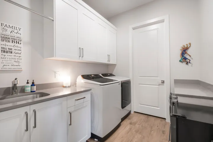 White cabinetry with brushed nickel hardware, stainless steel sink, wood-finish flooring, and light gray countertops