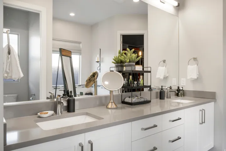 Dual vanity with integrated sinks, light gray countertop, white cabinetry with modern hardware, and wall-mounted mirror