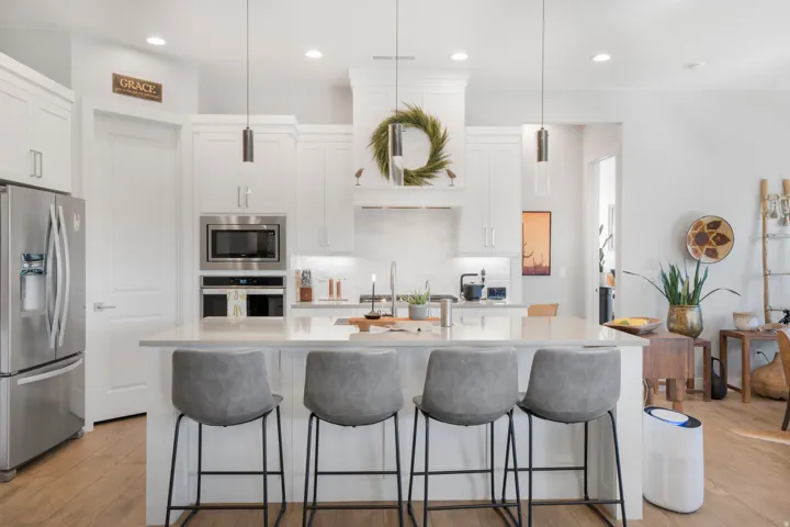 White shaker cabinetry, stainless steel appliances, central island with seating, pendant lighting, and wood-finish flooring