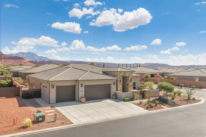 Stucco exterior with stone accents, concrete driveway, tiled roof, attached two-car garage, and desert-inspired landscaping