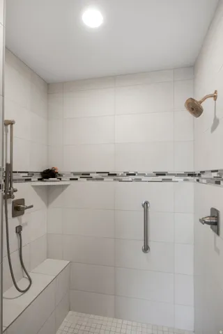 Tiled shower with a built-in bench, mosaic accent tile, handheld shower fixture, and a rain showerhead