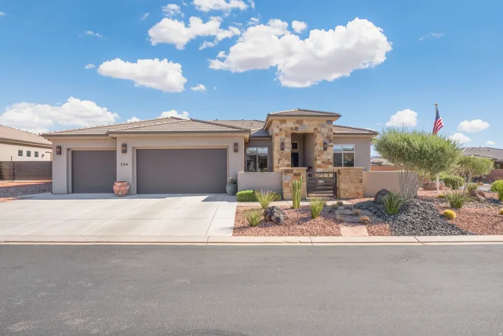 Stucco exterior with stone accents, an attached two-car garage, concrete driveway, and desert-style landscaping