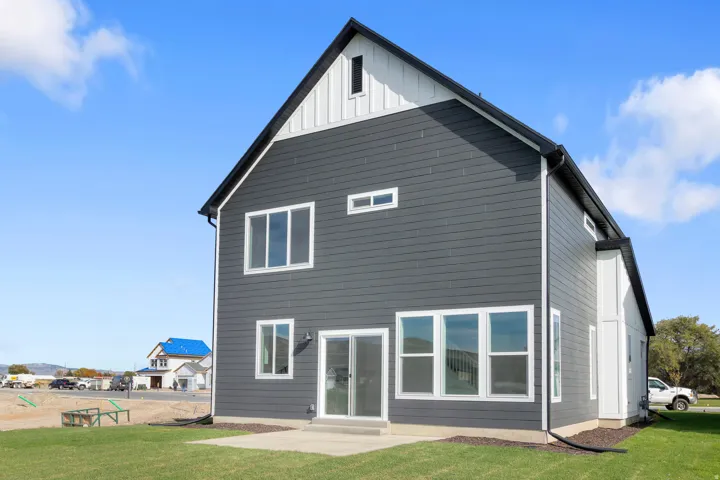 Dark gray horizontal siding with white trim, a black gabled roof, multiple white-framed windows, and a sliding glass door to a concrete patio