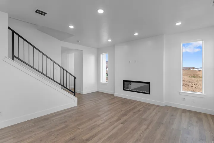Open-concept living space with wood-finish flooring, a contemporary linear fireplace, recessed lighting, and a modern staircase featuring black metal railings
