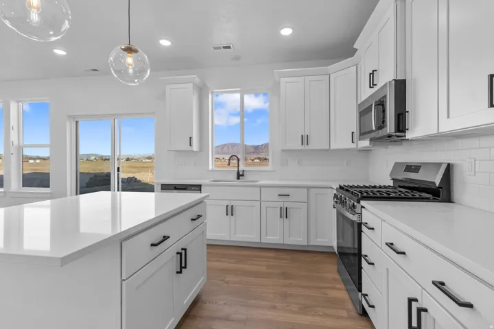 White shaker-style cabinetry with matte black hardware, white countertops, stainless steel appliances, and wood-finish flooring