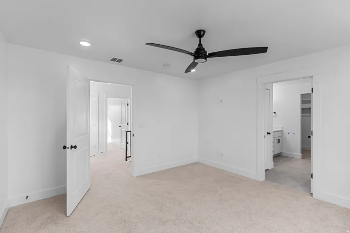 Neutral carpet flooring and white walls with a black ceiling fan