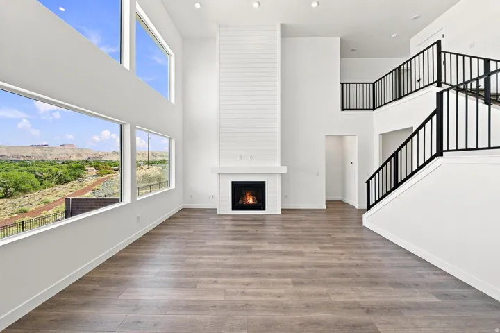 Two-story living space featuring an expansive window wall, wood-finish flooring, a shiplap-accented fireplace, and an open staircase with black metal railings