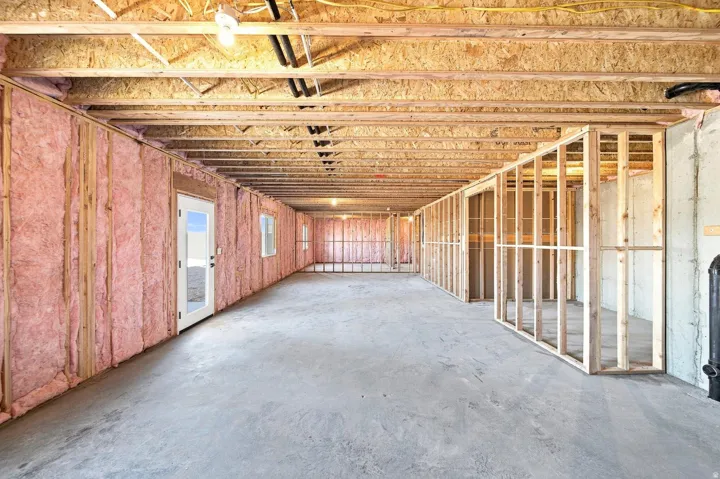 Unfinished lower level featuring exposed wood joists, framed interior walls, concrete flooring, and an exterior door with window