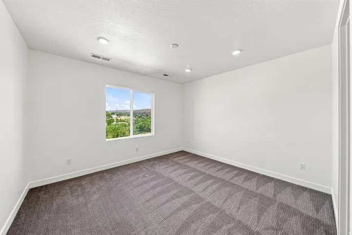 Recessed lighting, neutral wall paint, patterned carpeting, and a window with exterior scenery