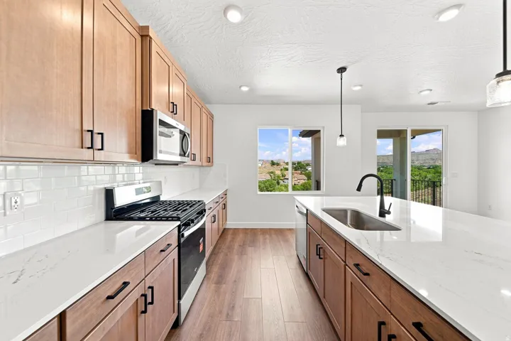 Kitchen featuring wood-finish cabinetry, white countertops, subway tile backsplash, stainless steel appliances, and a kitchen island with an undermount sink