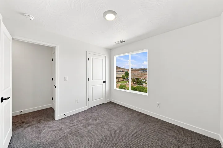 Neutral wall color with textured ceiling, dark gray carpeting, and white interior doors with black hardware
