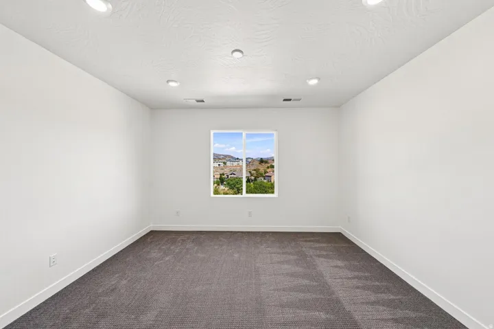 Recessed ceiling lighting, textured ceiling, light neutral wall paint, dark carpet flooring, and a single window