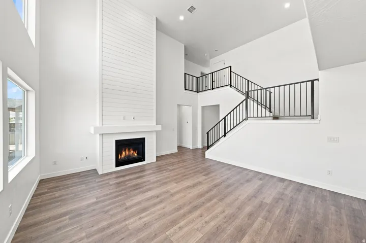 Two-story living area featuring a tall shiplap fireplace, wood-finish flooring, recessed lighting, and a multi-level staircase with black metal railings