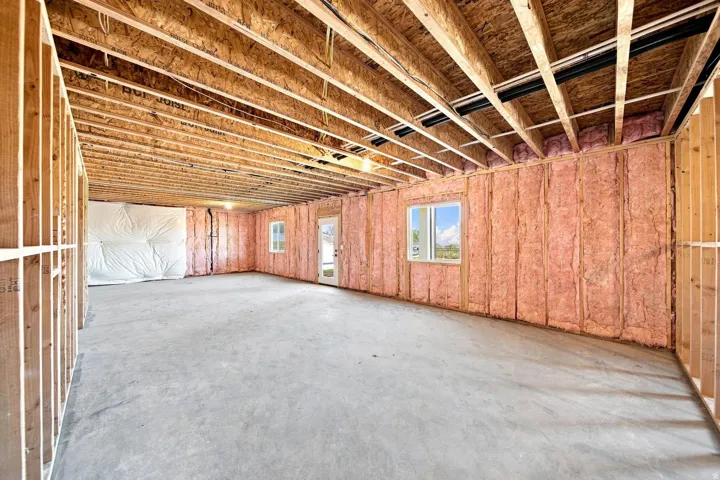 Unfinished basement space featuring exposed wood framing, concrete flooring, and an insulated exterior wall with a window